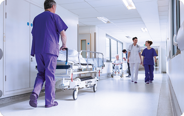 A picture of a hospital hallway with a nurse and doctor walking, a worker pushing a gurney, and a doctor talking to an elderly woman in a wheelchair