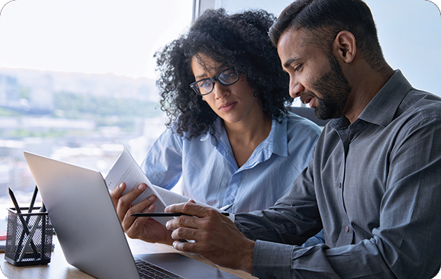 A picture of a man and woman reviewing documents in print outs and on a laptop during translation management.