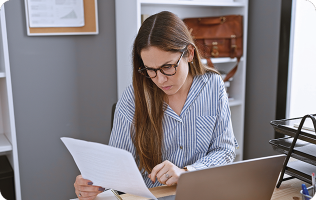 A picture of a female translator working on document translation for a mental health facility. She's reviewing paper documents and working on her laptop