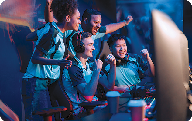 A picture of a group of e sports video game players cheering in front of a screen while one of their team plays the game.