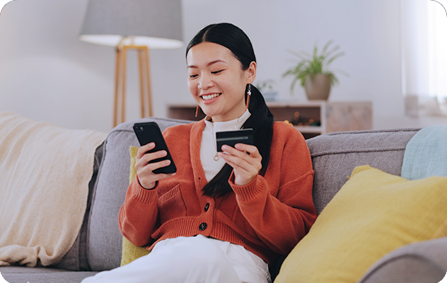 A picture of a young woman smiling while looking at her phone and holding a credit card