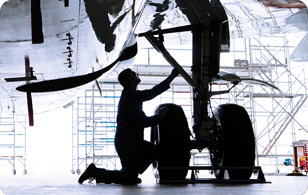 A picture of an aerospace worker inspecting a landing gear on a plane.