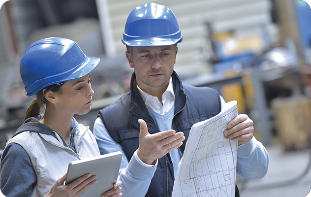 A man and a woman in hard hats looking at a set of translated blueprints in a manufacturing setting