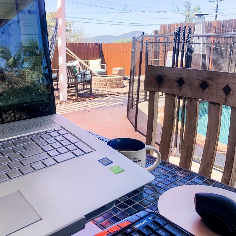 Laptop outside in front of a patio and pool with mountains in the background