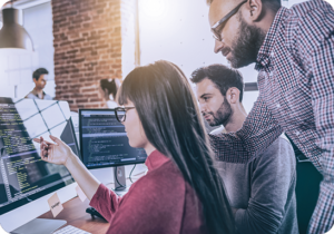 A picture of a team of three people view html code on a screen during website localization services.