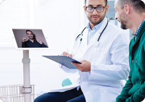 A picture of a doctor talking to a patient with a virtual interpreter present on a cart mounted computer tablet.