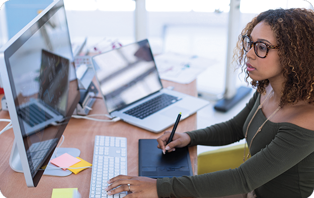 A female designer working on multilingual desktop publishing on a desktop computer while using an interactive drawing tablet