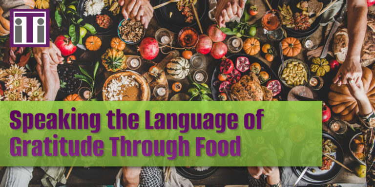 An image from above of a large table filled with food and some hands reaching across the table. Title reads speaking the language of gratitude through food.